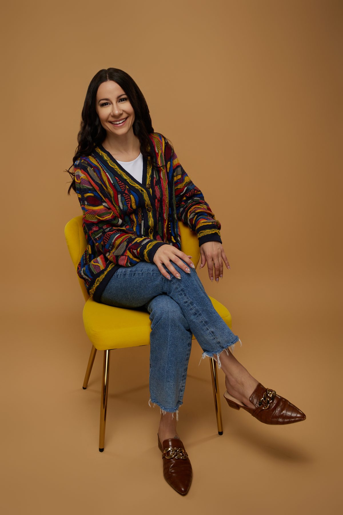 Bryanna Baptiste in her Coogi cardigan, seated in a yellow chair against a caramel backdrop