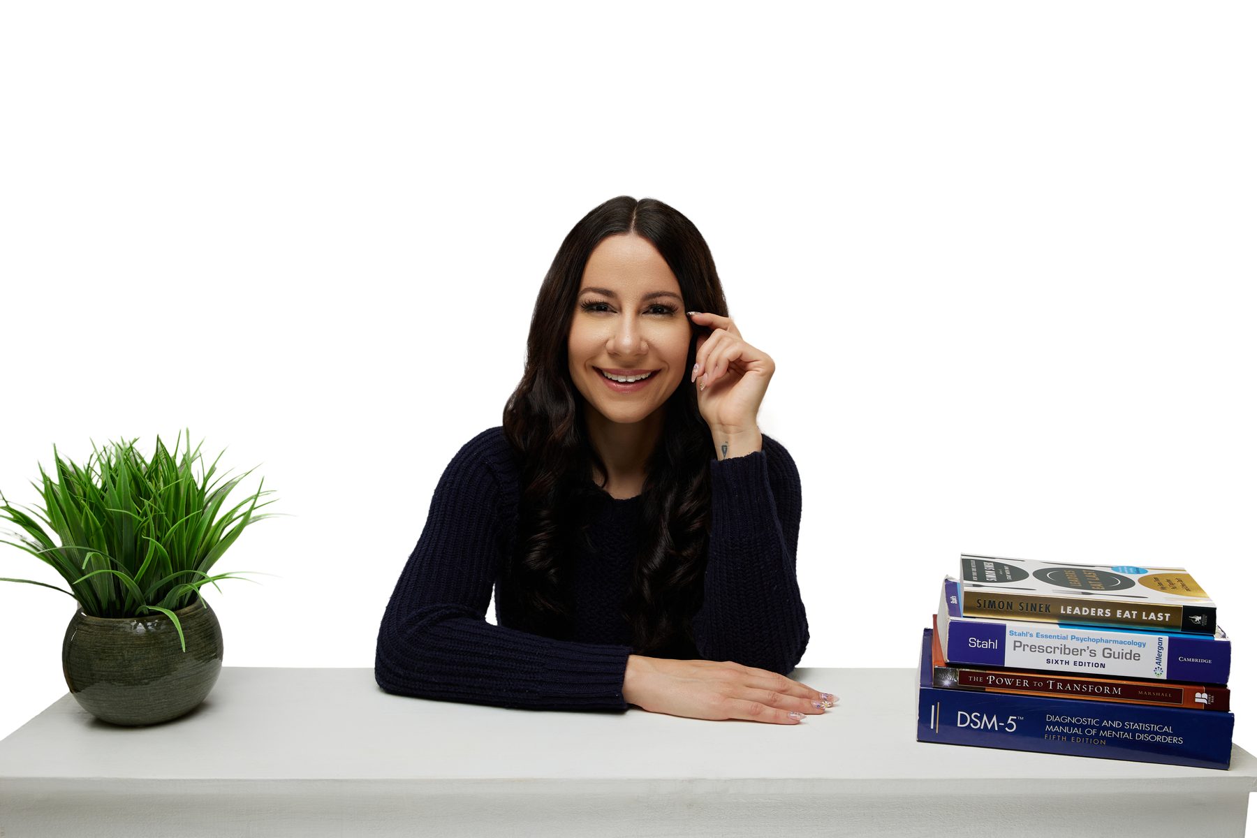 Bryanna Baptiste in a navy sweater, seated at a desk stacked with books